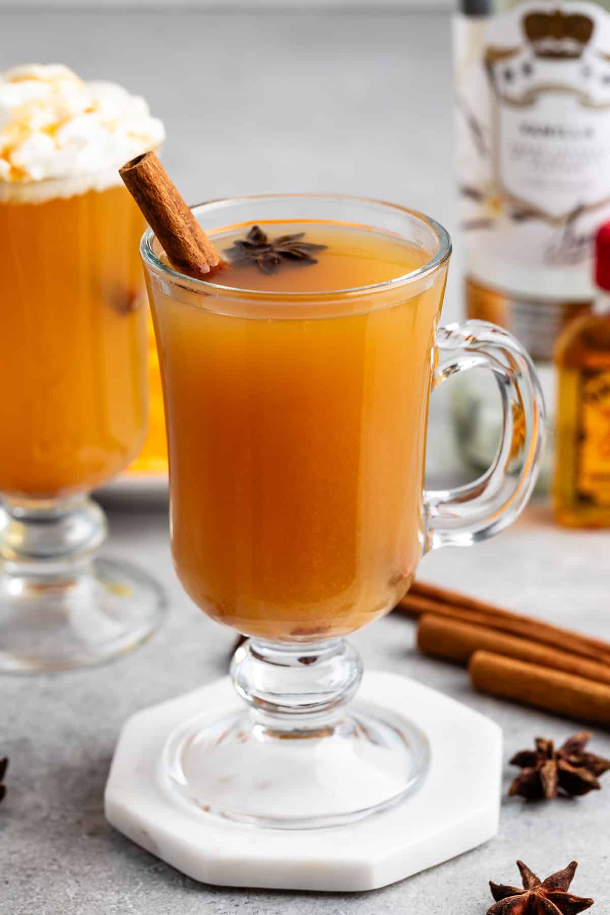 apple cider in a clear glass with a handle and a cinnamon stick on the top.