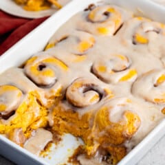 pumpkin cinnamon roll covered in glaze and cinnamon on a white pan.