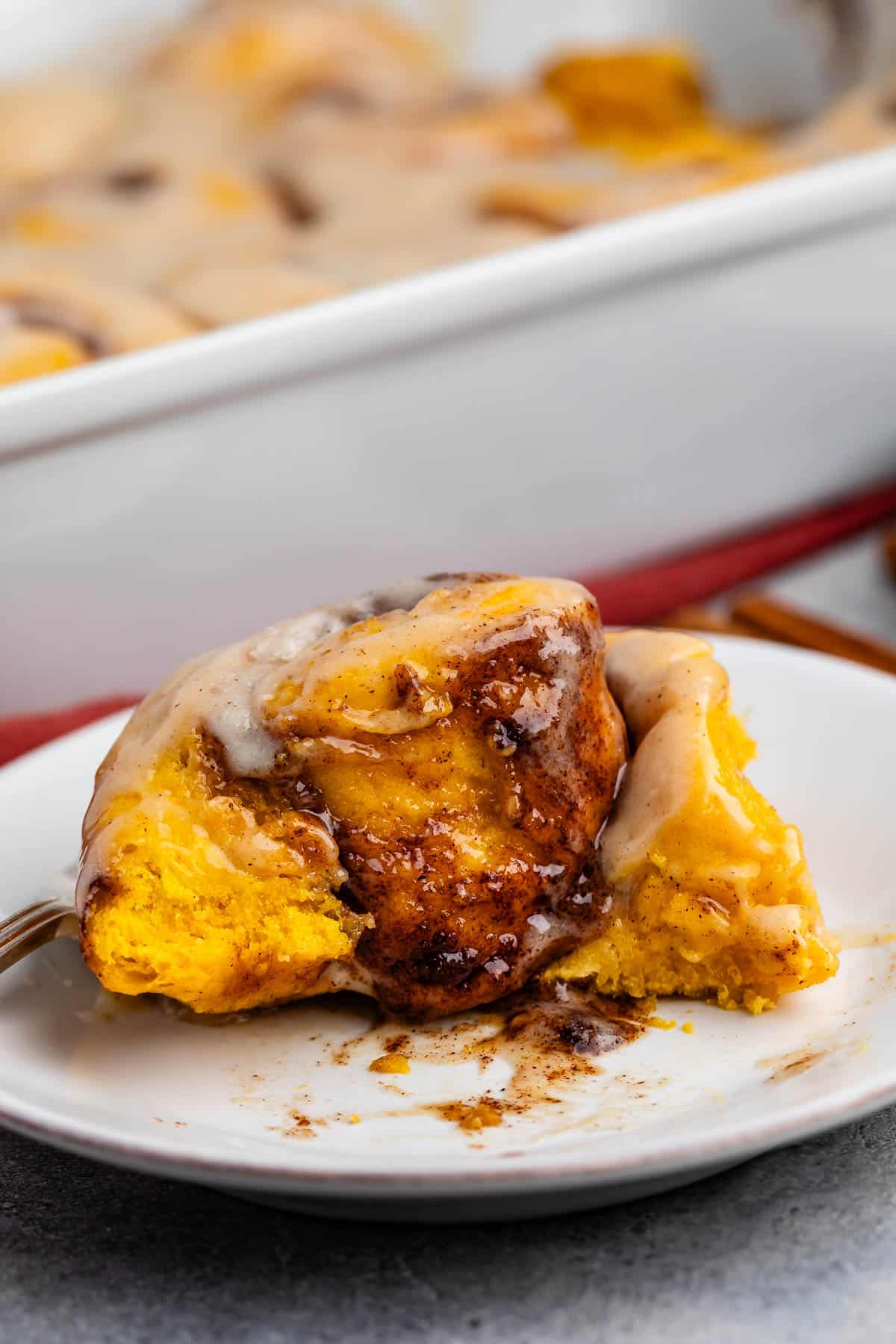 pumpkin cinnamon roll covered in glaze and cinnamon on a white plate.