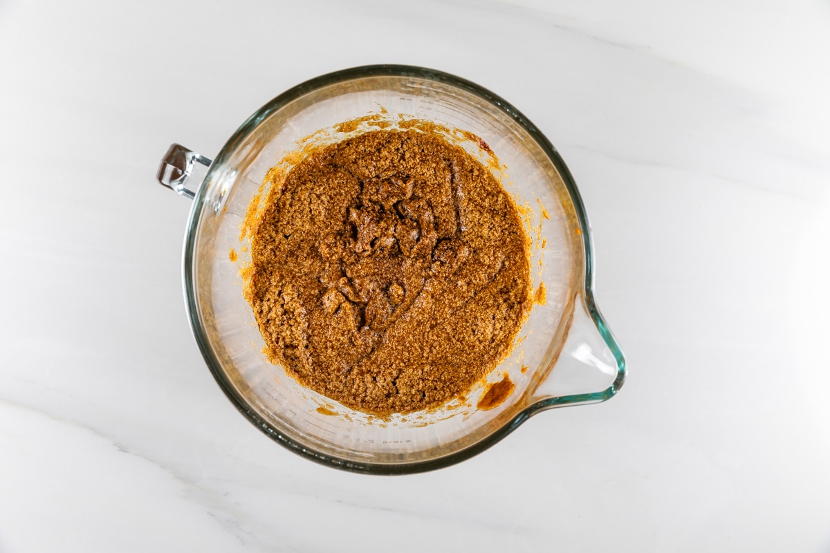 A glass mixing bowl filled with a crumbly brown mixture, set on a white marble countertop.