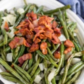 green beans in a white bowl topped with bacon and onions.