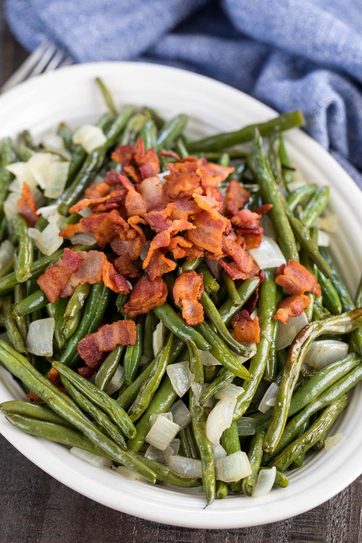 green beans in a white bowl topped with bacon and onions.