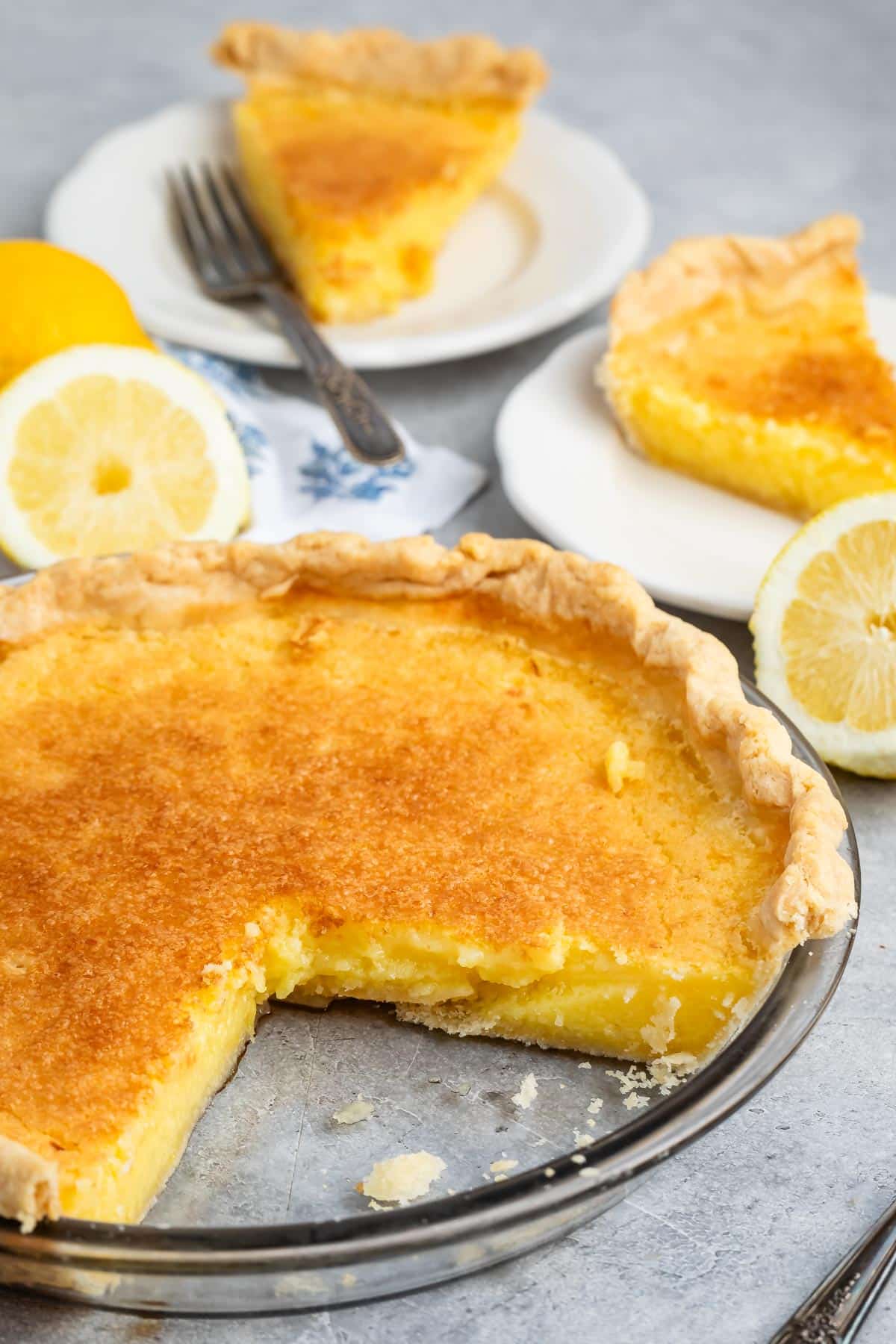 lemon chess pie one a white plate with a sliced lemon in the back.