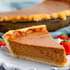 slice of pumpkin pie on a grey plate next to a candy corn pumpkin.