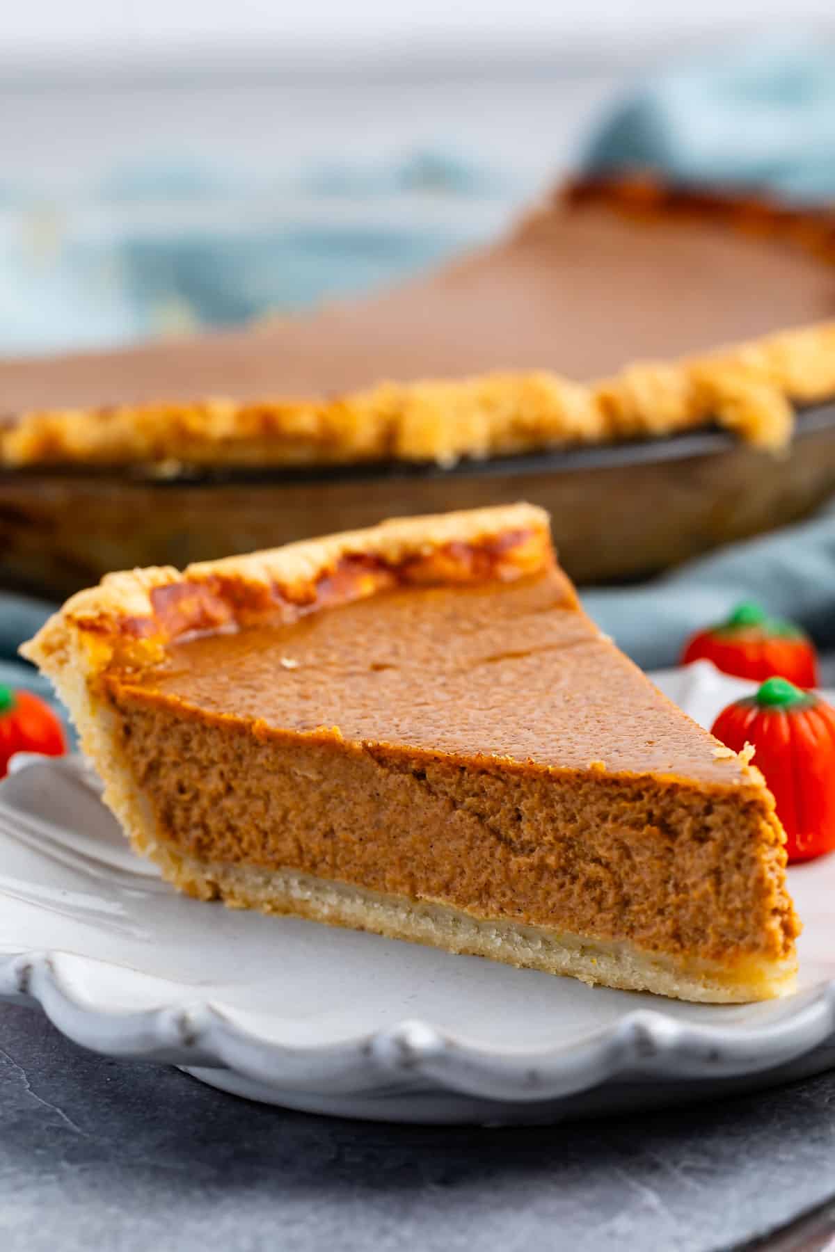 slice of pumpkin pie on a grey plate next to a candy corn pumpkin.