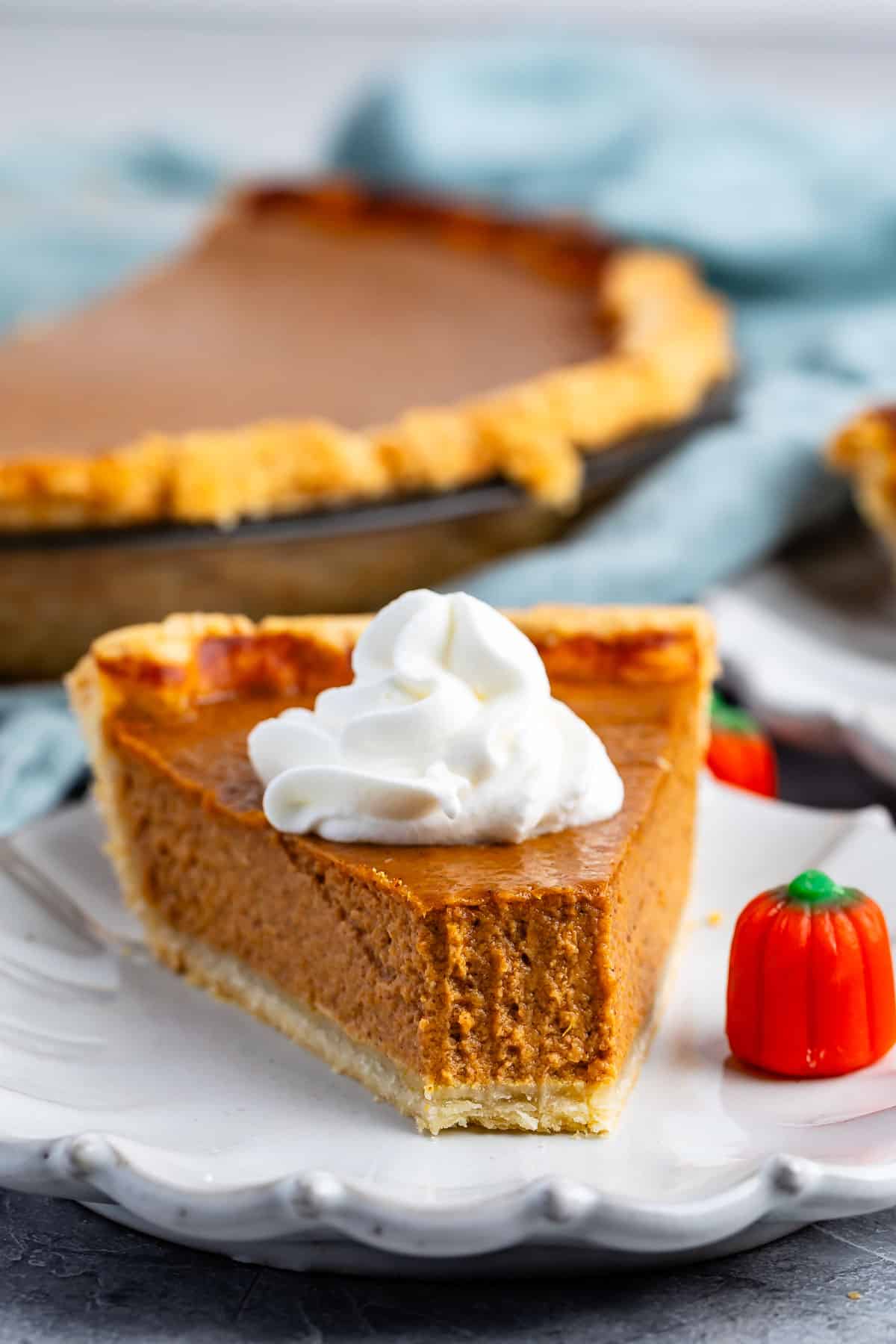 slice of pumpkin pie on a grey plate next to a candy corn pumpkin.