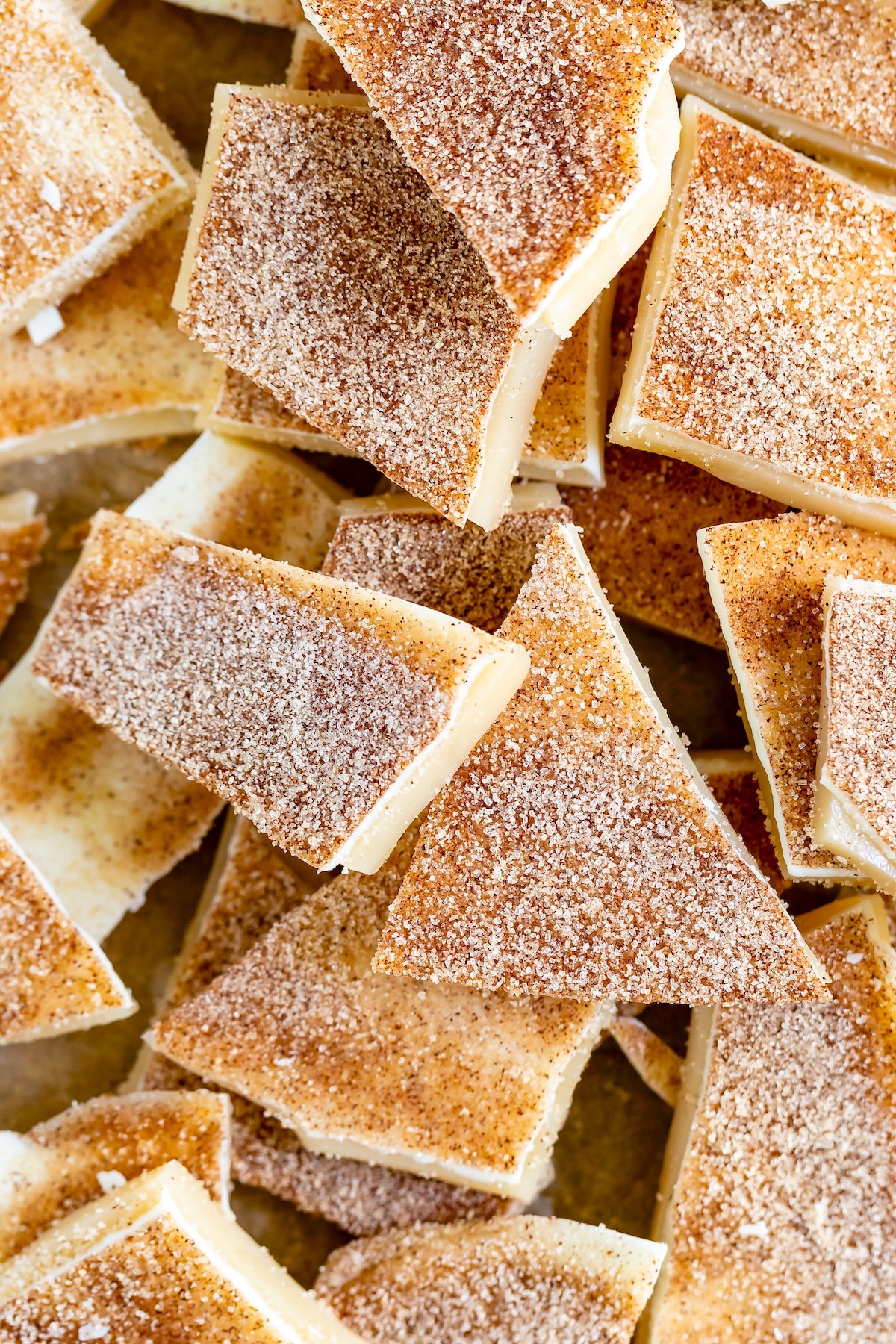 A pile of cinnamon sugar covered crackers, golden brown and dusted with sugar and cinnamon, are stacked haphazardly. The crackers have a crisp texture and a sweet, spiced appearance.