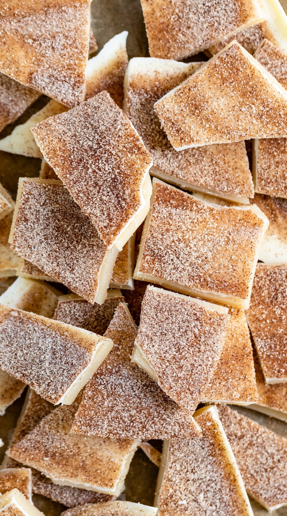 A close-up of several pieces of cinnamon sugar bark, featuring unevenly cut squares and triangles. The bark has a creamy white base layer topped with a generous dusting of cinnamon and sugar.