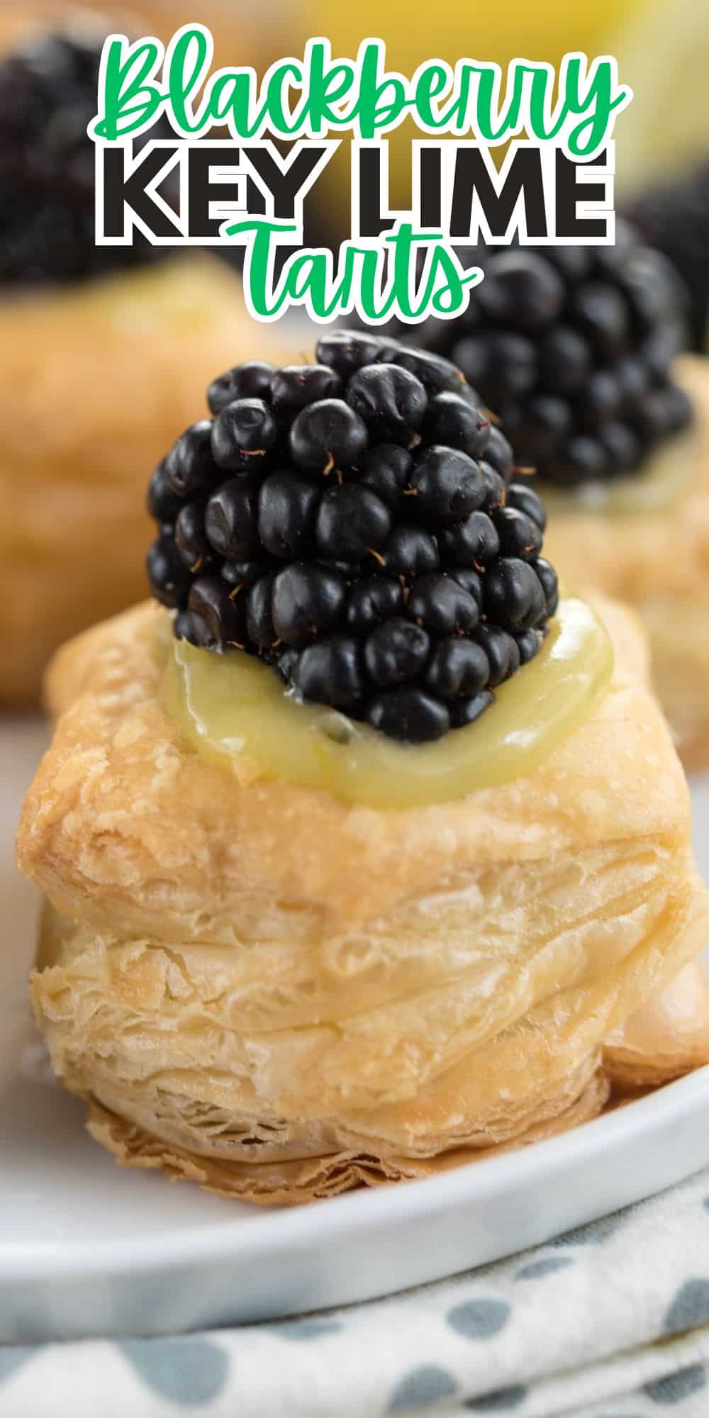 A close-up of a pastry topped with green key lime filling and a fresh blackberry. Text above reads Blackberry Key Lime Tarts. The background features more pastries on a white plate.