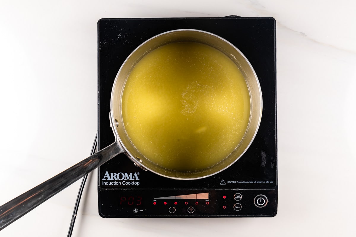 A pot with green liquid is on an induction cooktop, displaying P03 on the control panel, indicating a low-temperature setting. The cooktop is black with red digital numbers.