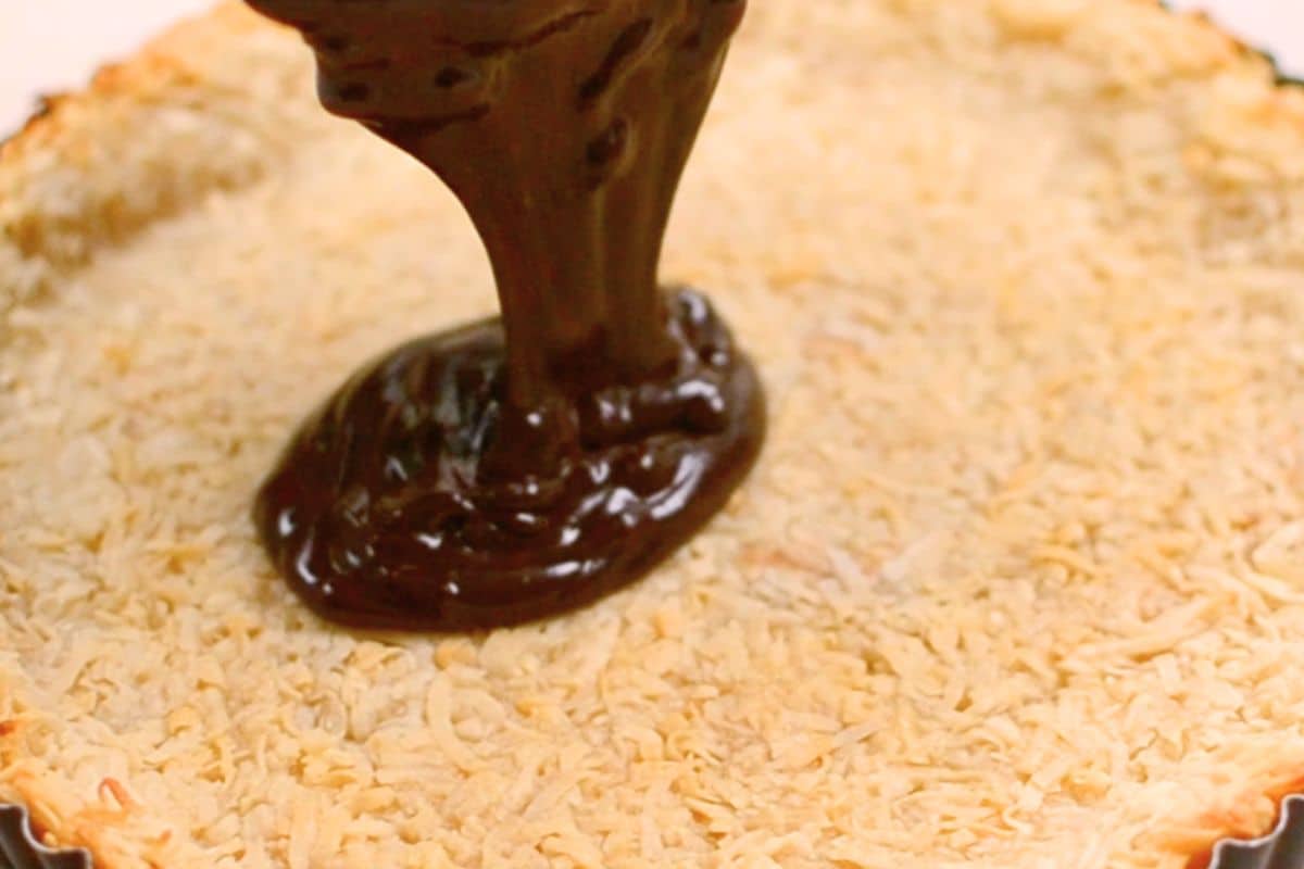 Chocolate being poured onto a crust topped with shredded coconut.