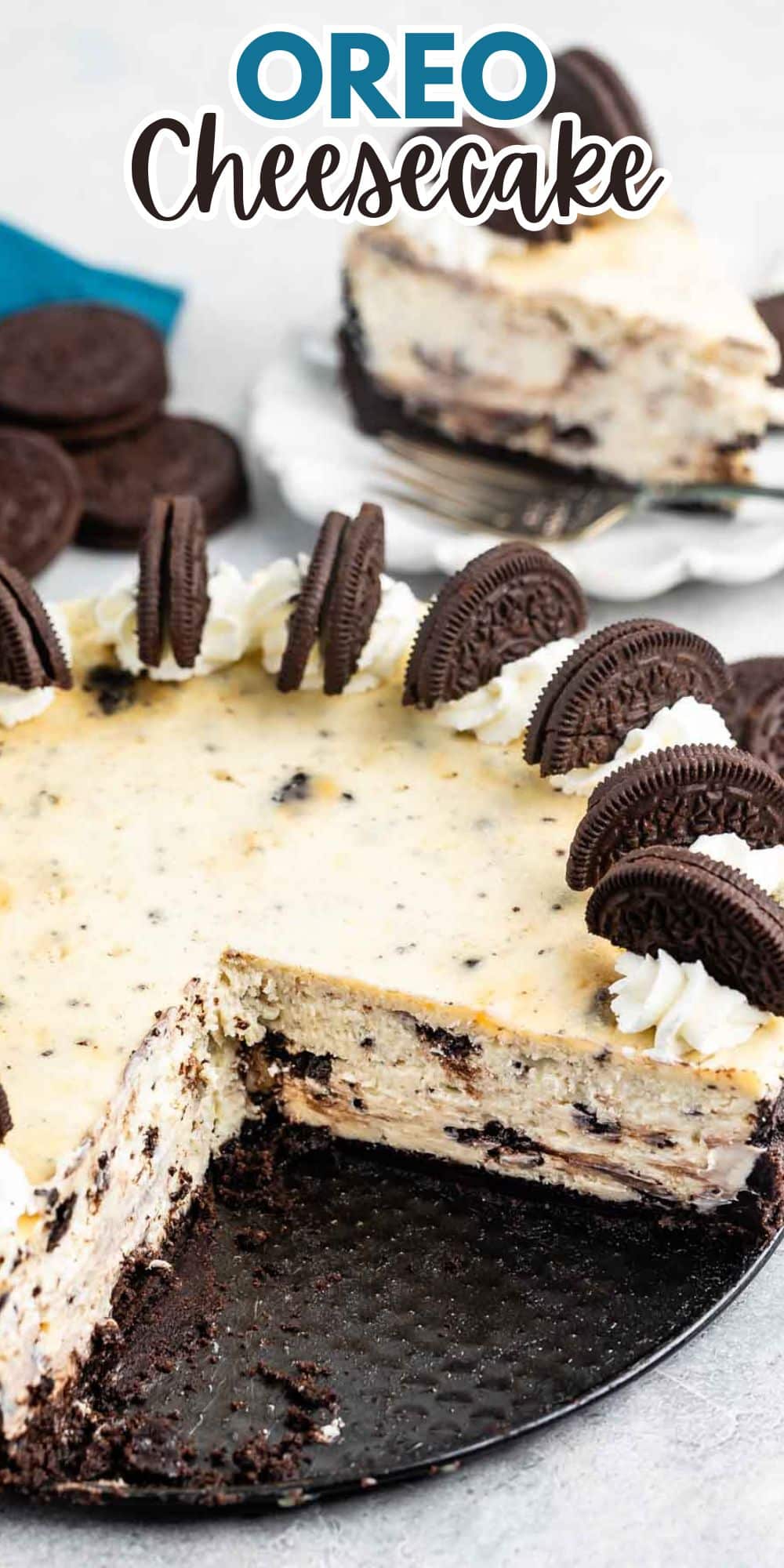 A creamy Oreo cheesecake with a slice removed, revealing a rich texture. The top is garnished with halved Oreo cookies and dollops of whipped cream. A separate slice with a fork is visible in the background.