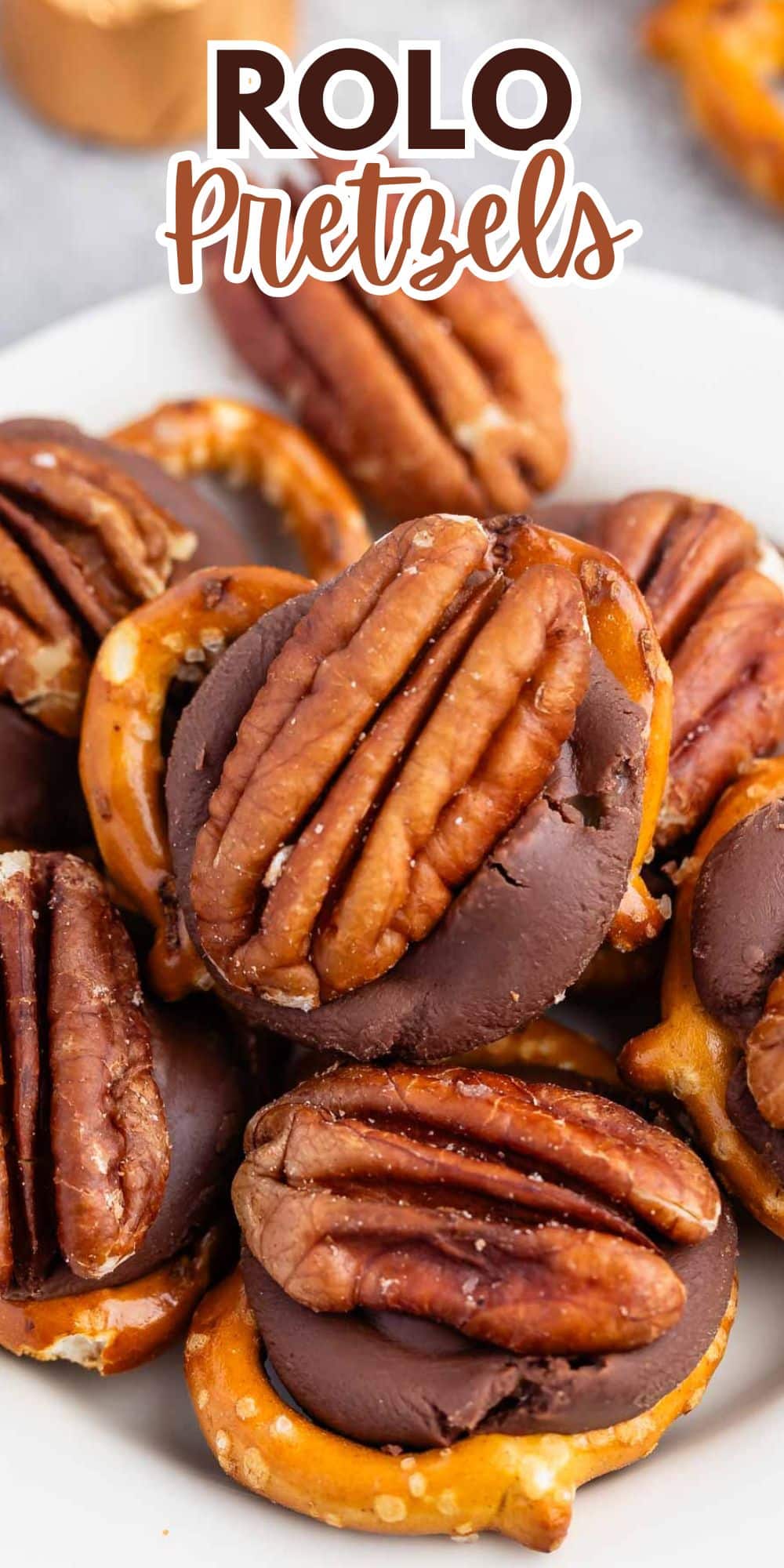 Close-up of Rolo pretzels topped with pecans on a white plate. Pretzels are partially covered with melted chocolate and caramel, with pecans placed on top. Text at the top reads Rolo Pretzels.