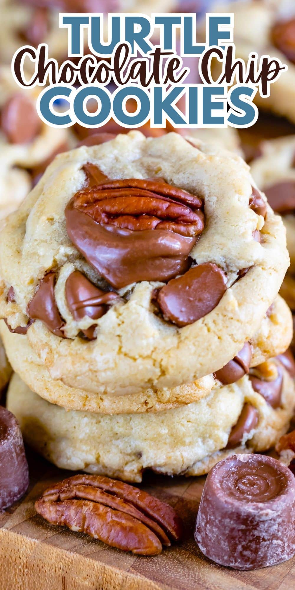 Close-up of turtle chocolate chip cookies topped with pecan halves and chocolate pieces. The text Turtle Chocolate Chip Cookies is visible above the cookies. The cookies are stacked on a wooden surface.