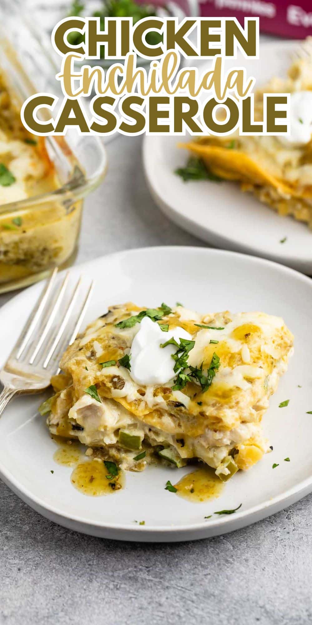 A slice of chicken enchilada casserole on a white plate, topped with sour cream and chopped cilantro, with a fork on the side. Another plate and a glass baking dish with more casserole are in the background. Text reads Chicken Enchilada Casserole.