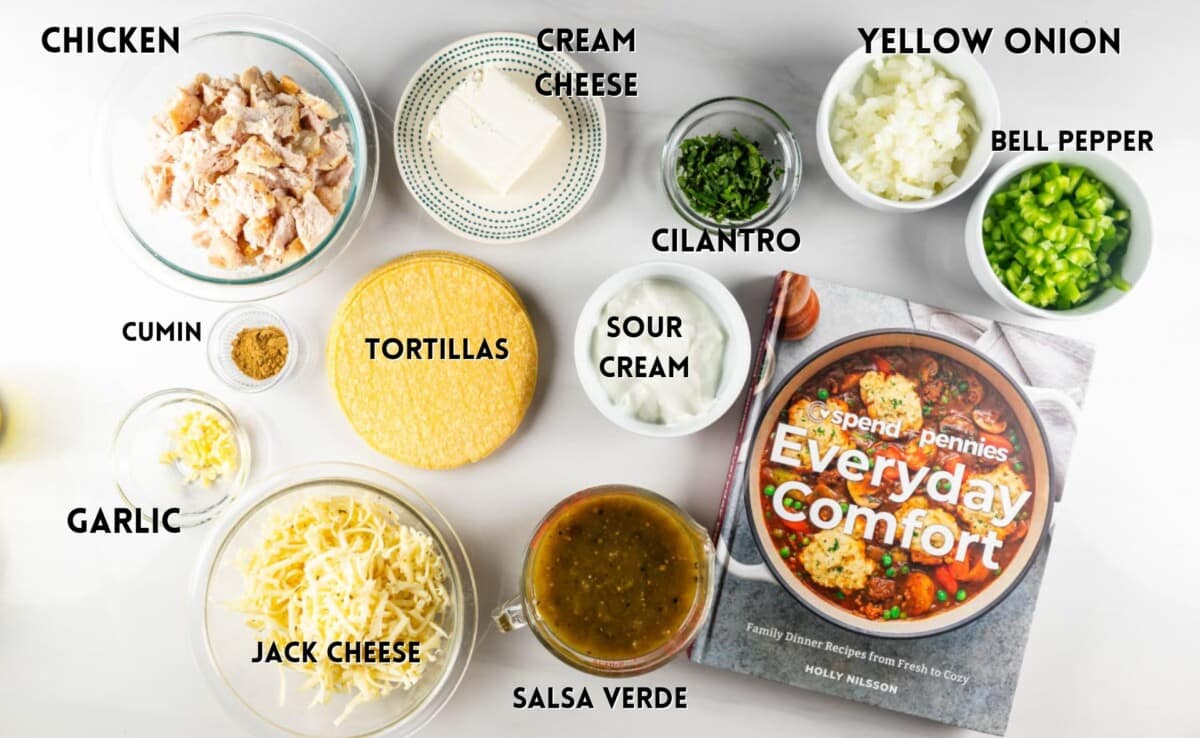 A flat lay of ingredients labeled: shredded chicken, cumin, garlic, jack cheese, tortillas, salsa verde, sour cream, cream cheese, cilantro, yellow onion, and bell pepper. A cookbook titled Everyday Comfort is also visible.