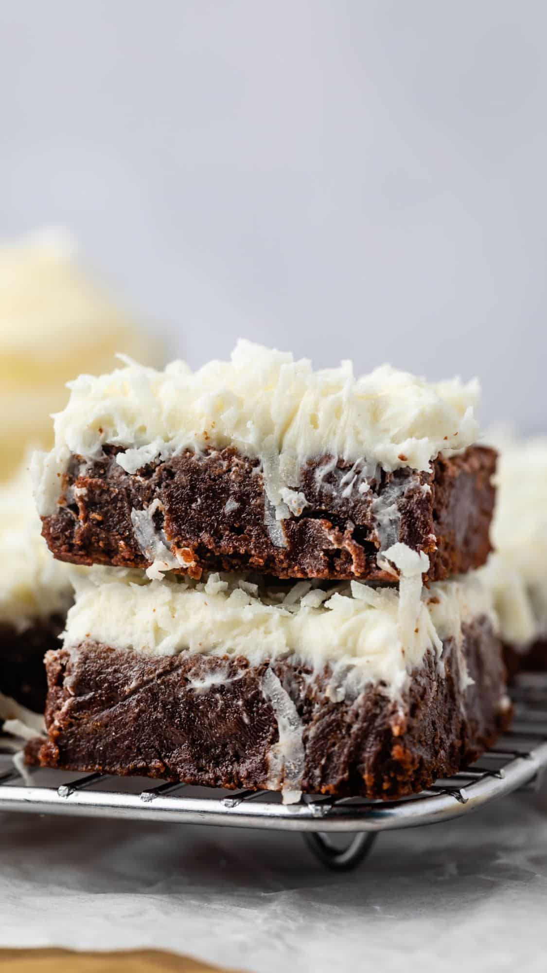 stacked brownies with coconut and white frosting on top.