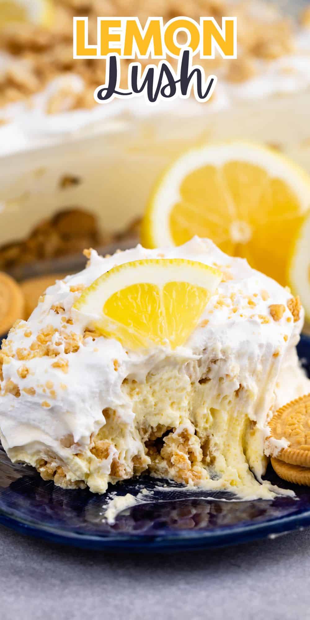 A slice of lemon lush dessert on a dark plate, topped with whipped cream and a lemon slice. The dessert is garnished with crumbled cookies, and additional lemon slices and cookies are scattered around.