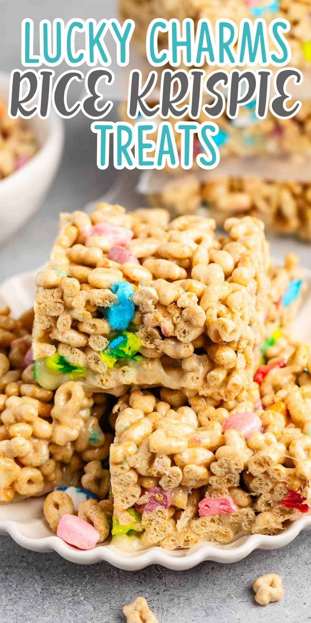 Close-up of Rice Krispie treats mixed with Lucky Charms cereal, stacked on a white plate. The colorful marshmallows and cereal bits are prominent, creating a playful and appetizing appearance. Text above reads, Lucky Charms Rice Krispie Treats.