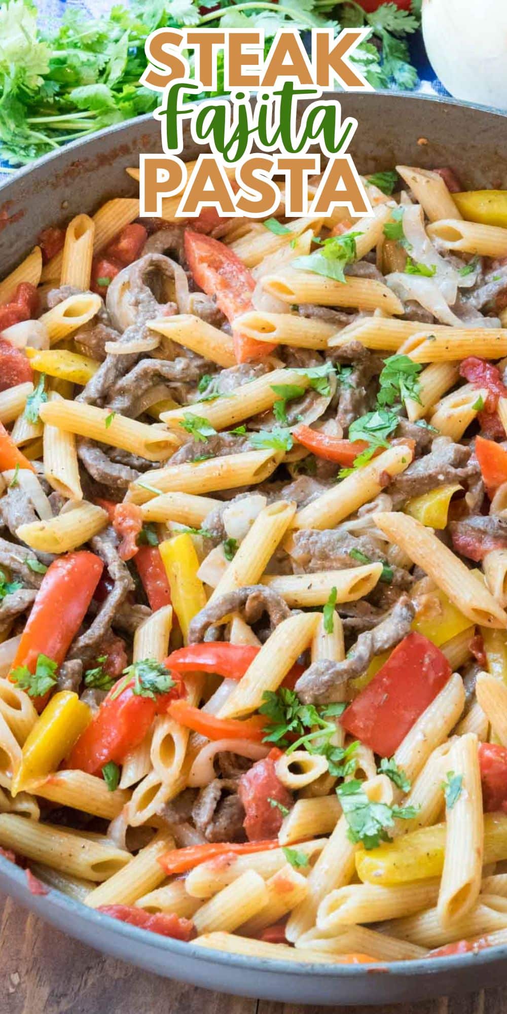 A close-up of steak fajita pasta in a pan, featuring penne pasta, strips of steak, red and yellow bell peppers, and garnished with fresh cilantro. Text overlay reads Steak Fajita Pasta at the top.