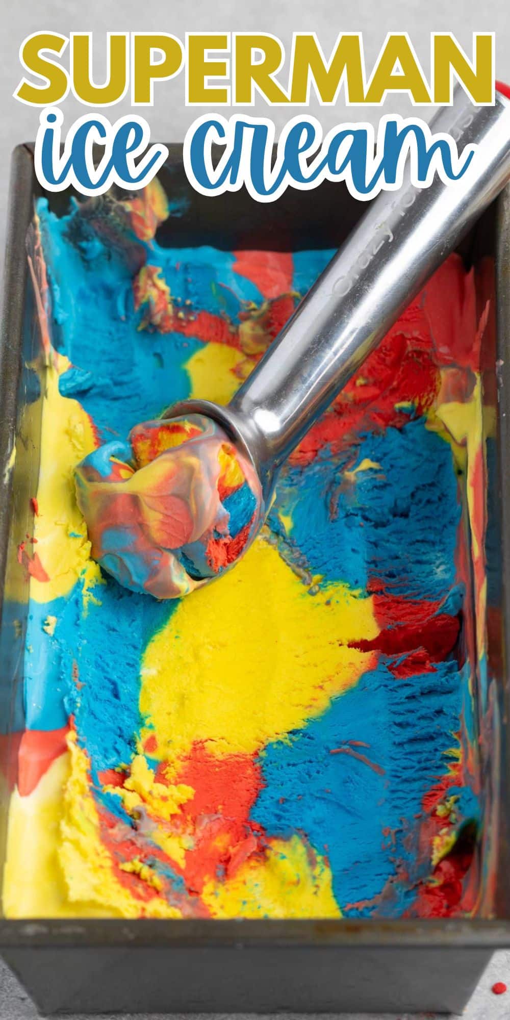 A pan of colorful Superman ice cream with vibrant swirls of blue, red, and yellow. A metal ice cream scoop is placed on top, filled with a mix of the three colors.