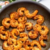 Sautéed shrimp with a golden-brown crust in a pan, seasoned with spices. Fresh parsley and a striped towel are slightly visible in the background.