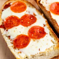 A close-up of French bread pizza topped with melted cheese and pepperoni slices. The bread is toasted, and the pizza is sprinkled with herbs. It rests on a wooden surface.