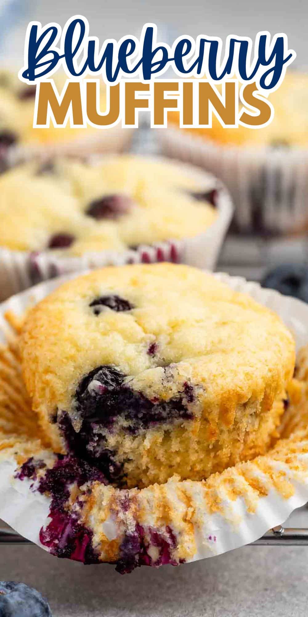 Close-up of a freshly baked blueberry muffin with visible blueberries, partially unwrapped from its paper liner. The background shows more muffins, and the words Blueberry Muffins are displayed at the top.