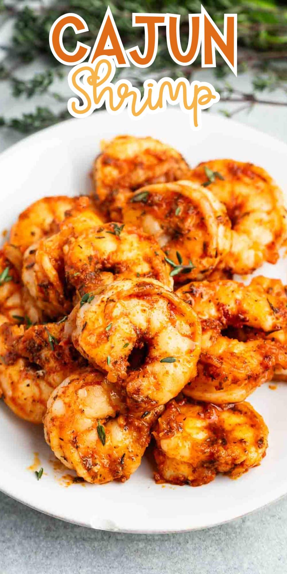 A white plate filled with seasoned Cajun shrimp is garnished with herbs. The text Cajun Shrimp is above the dish. The vibrant orange and red hues suggest a spicy, flavorful dish.