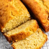 Two loaves of banana bread on a cooling rack, with one loaf partially sliced. The bread has a golden-brown crust and a moist, textured interior.