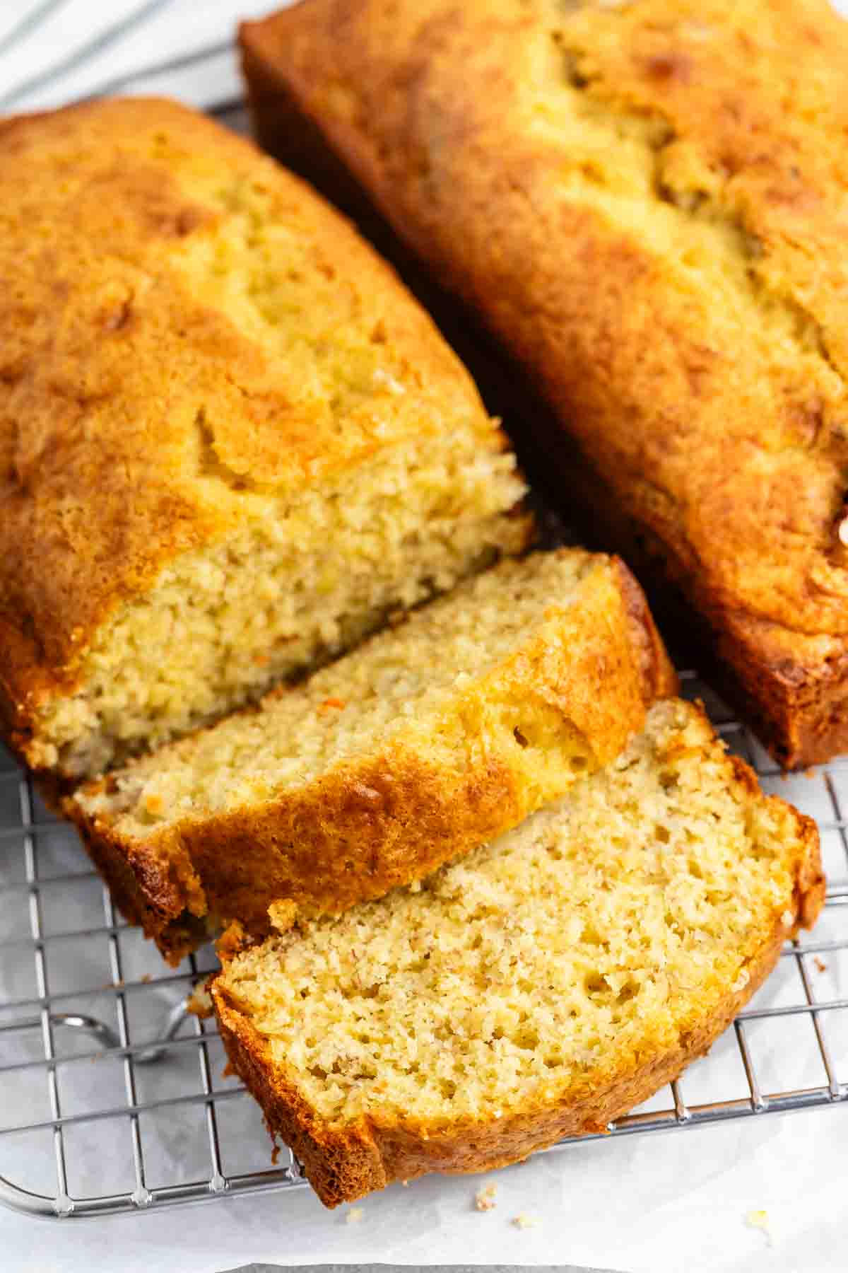 Two loaves of banana bread on a cooling rack, with one loaf partially sliced. The bread has a golden-brown crust and a moist, textured interior.