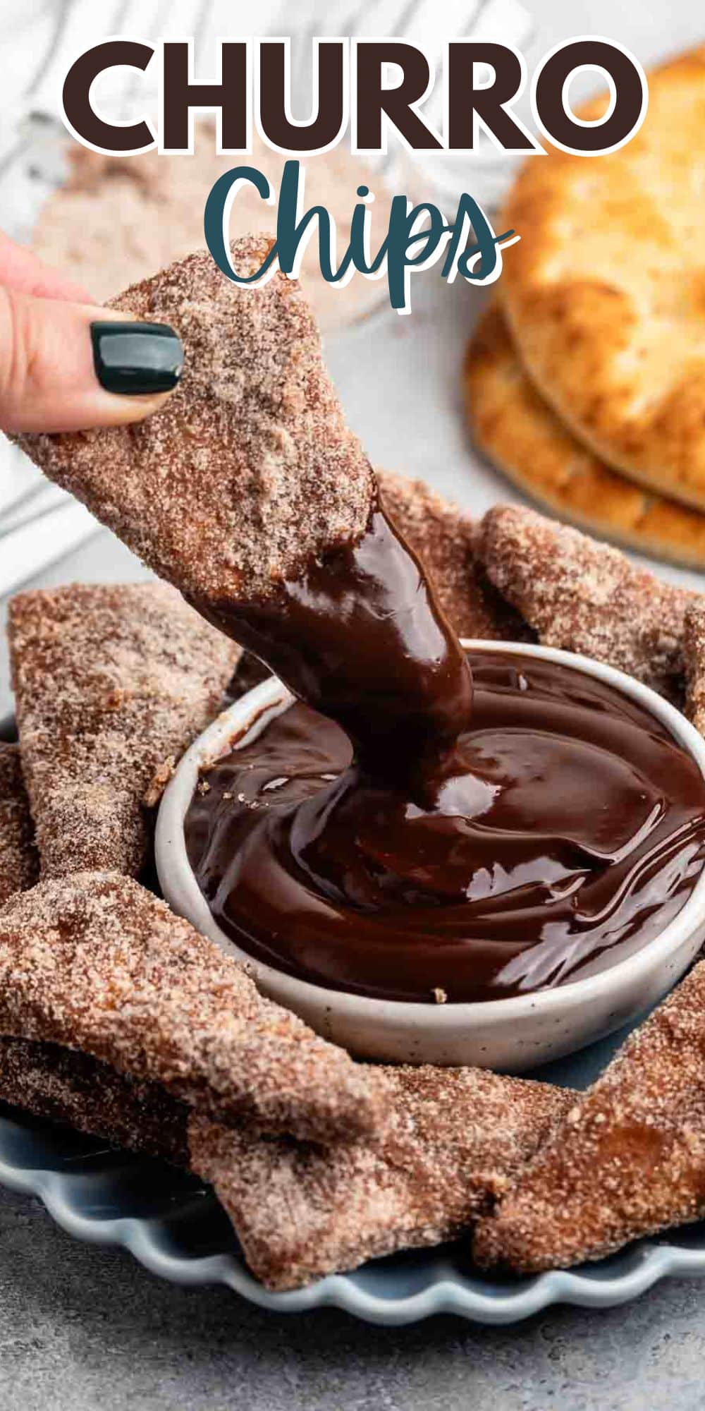 A hand dips a cinnamon-sugar churro chip into a bowl of melted chocolate. A plate is filled with more churro chips, and a stack of tortillas is visible in the background. The text Churro Chips is at the top.