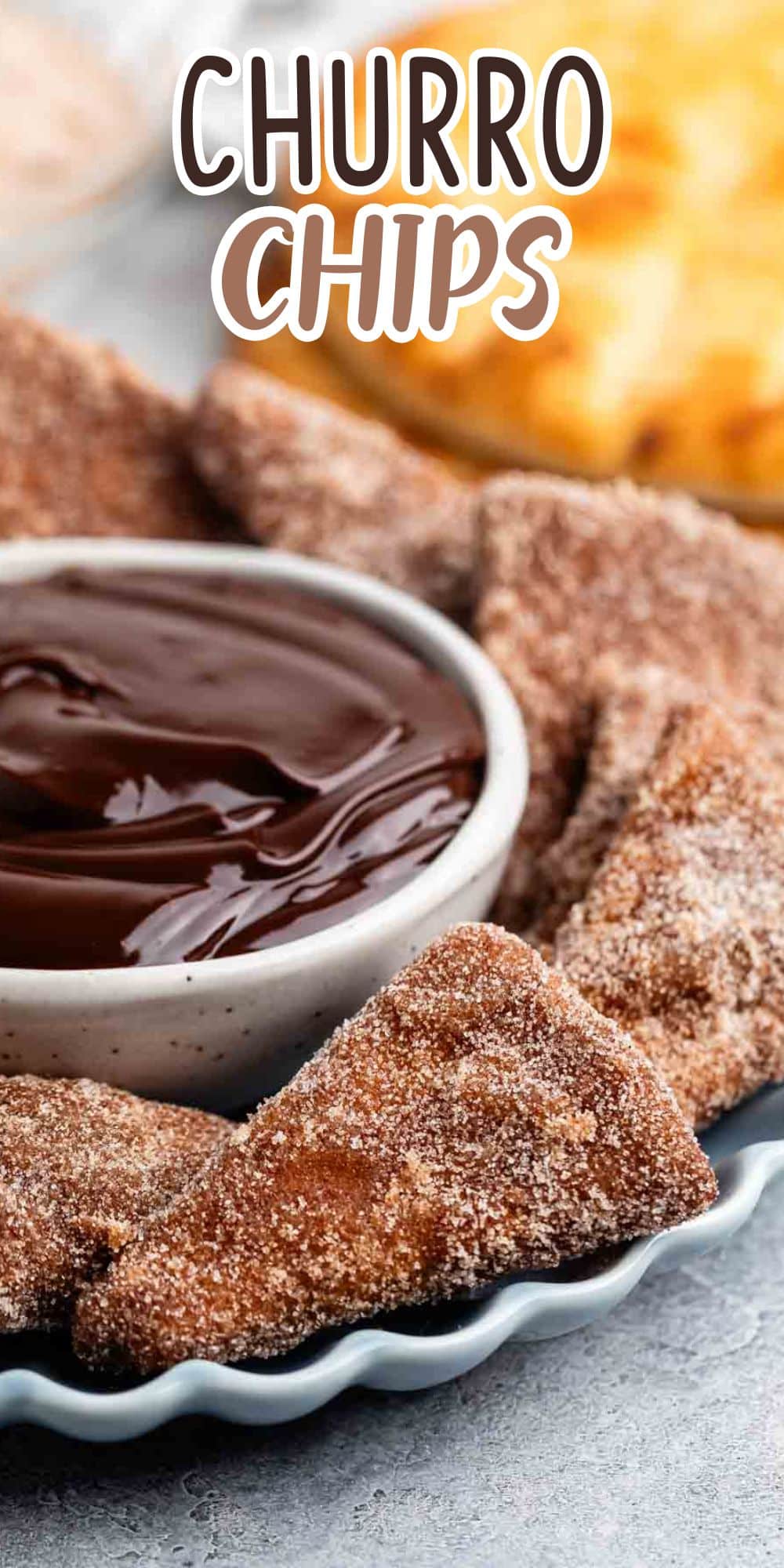 Churro chips dusted with cinnamon and sugar, arranged on a plate with a bowl of rich chocolate sauce for dipping.