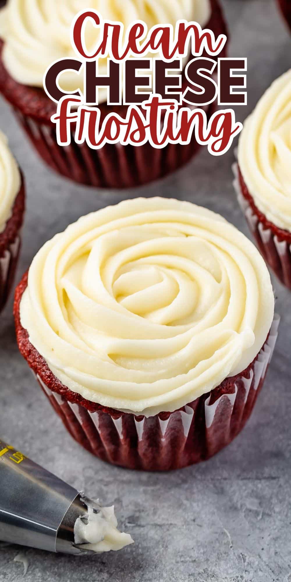 Red velvet cupcakes topped with creamy, swirled cream cheese frosting. A piping bag with frosting is nearby. Text above reads Cream Cheese Frosting. The background is a gray, textured surface.