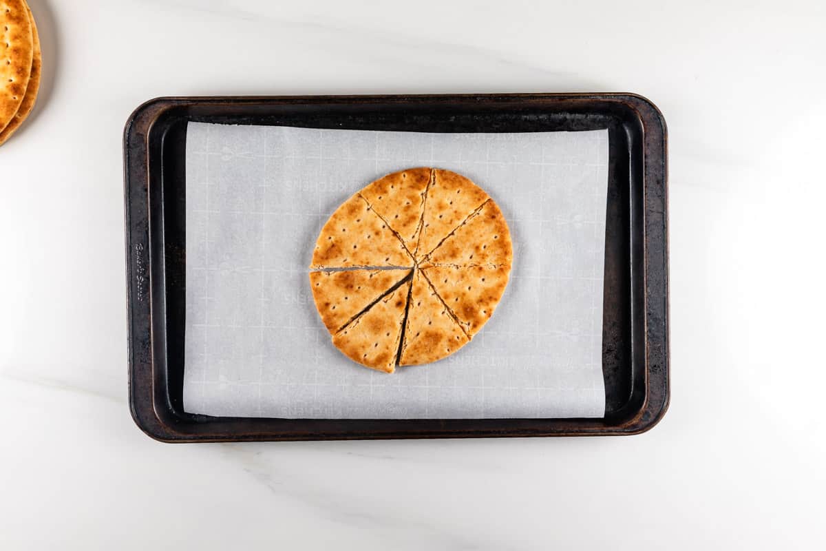 A round cornbread cut into eight slices sits on a baking sheet lined with parchment paper. The baking sheet is placed on a white marble surface.