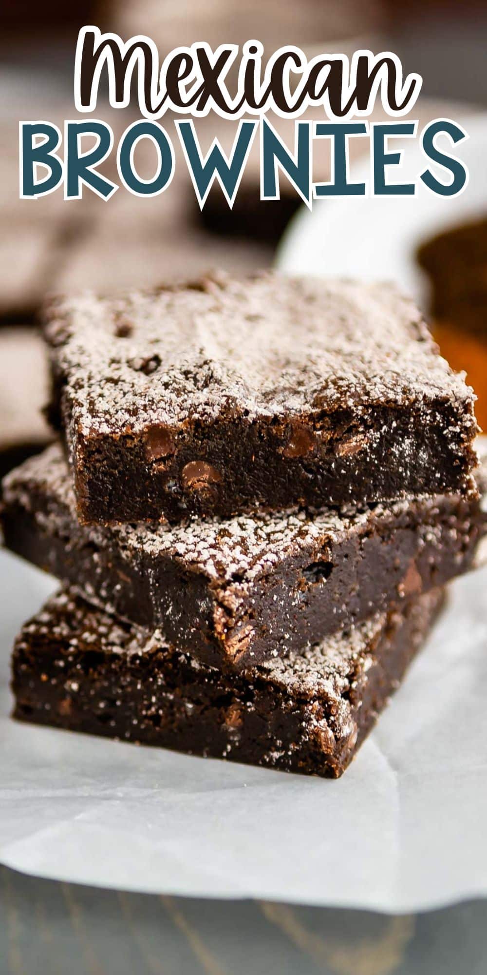 A stack of three chocolate brownies dusted with powdered sugar is placed on white parchment paper. Text reads Mexican Brownies at the top.