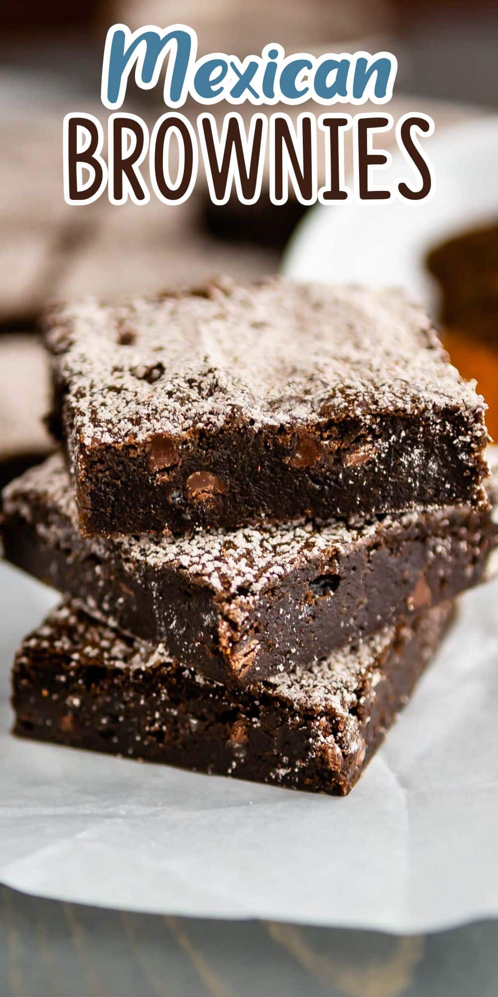 A stack of Mexican brownies topped with powdered sugar is displayed on a piece of parchment paper. The brownies are rich and chocolatey, with visible chocolate chips, creating a tempting dessert presentation. Mexican Brownies text is at the top.