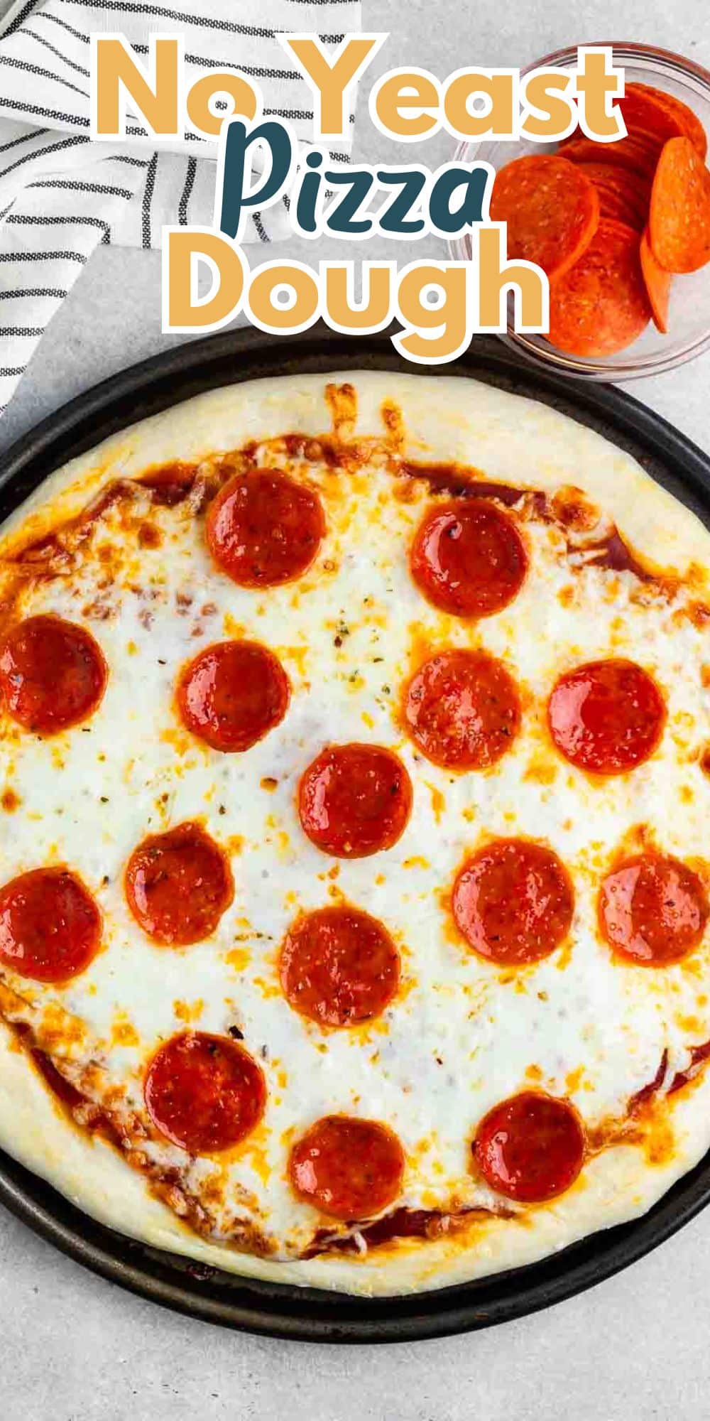 A pepperoni pizza with melted cheese is on a round black baking tray. No Yeast Pizza Dough is written in bold at the top. In the background, theres a small bowl with pepperoni slices and a striped towel.