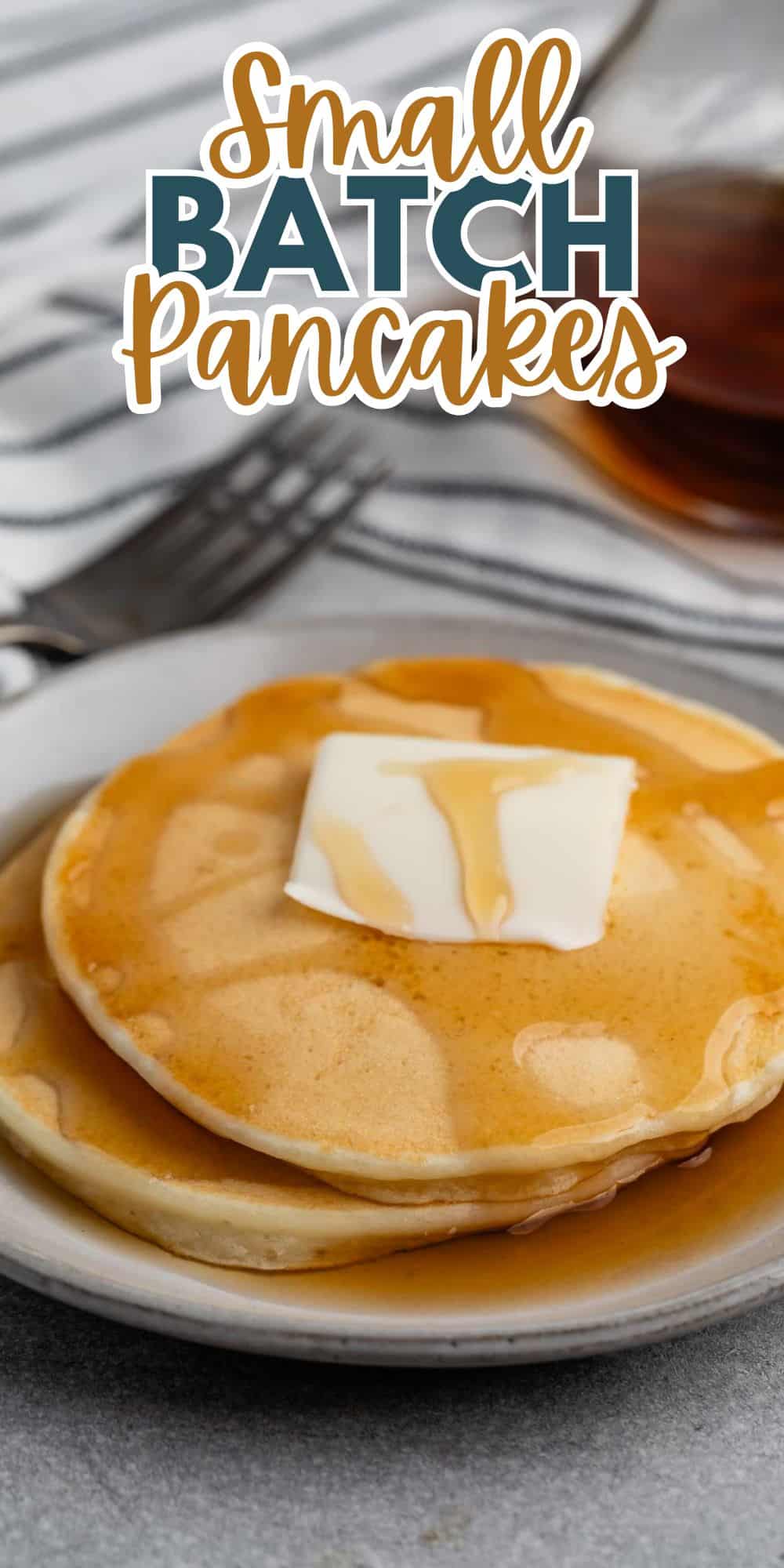 A close-up of two pancakes topped with butter and syrup on a white plate. A fork and a glass of syrup are in the background. Text at the top reads Small Batch Pancakes.