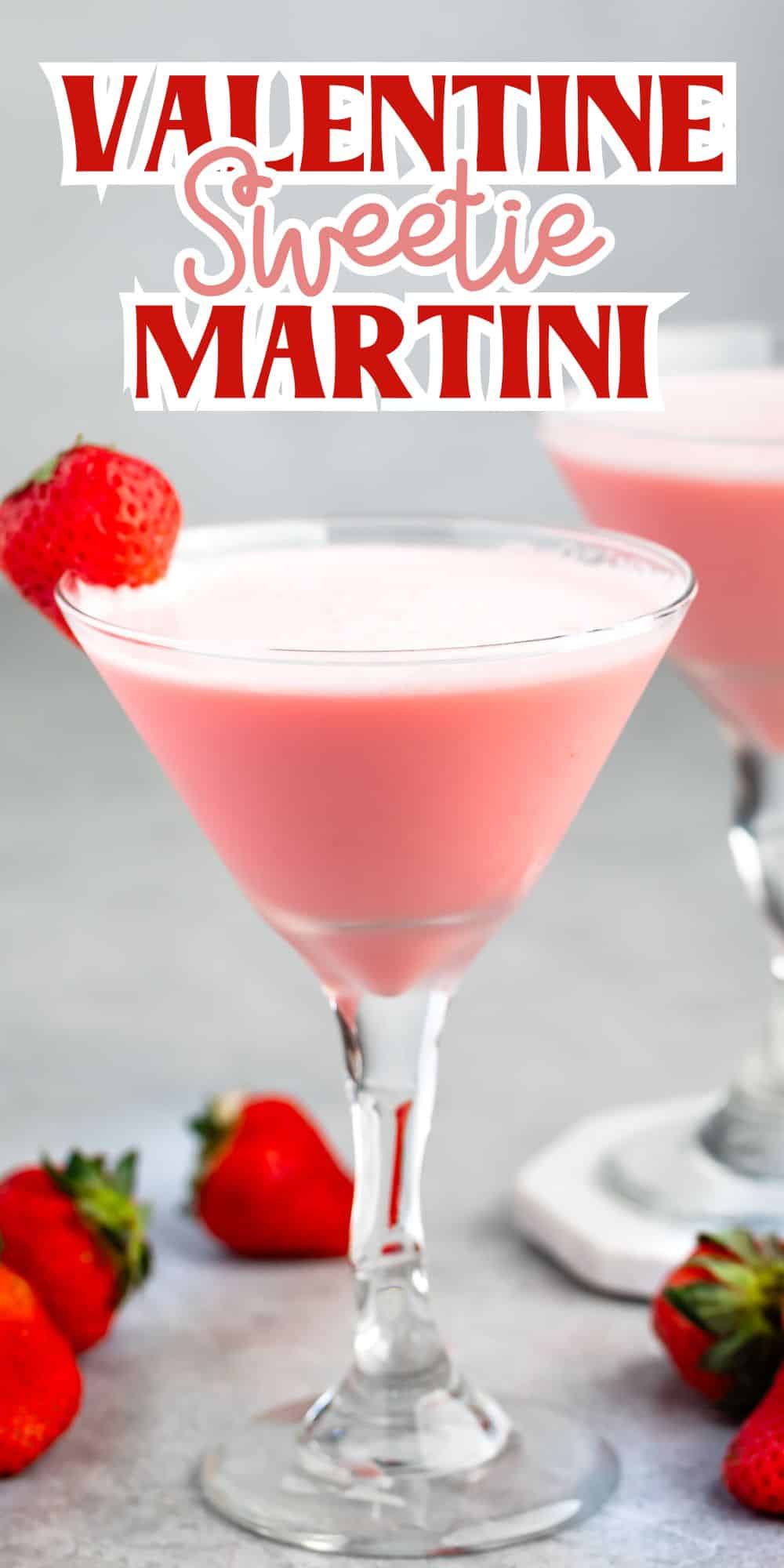 A pink cocktail in a martini glass is garnished with a strawberry on the rim. The background features strawberries scattered on a grey surface. Text above reads Valentine Sweetie Martini in red and white letters.