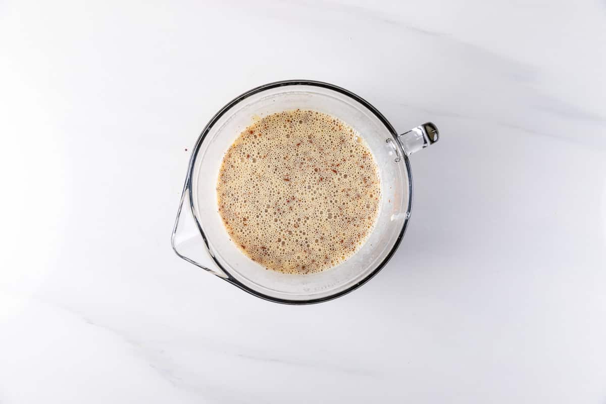 A top-down view of a glass measuring cup filled with a light brown liquid containing tiny specks, sitting on a white marble surface.