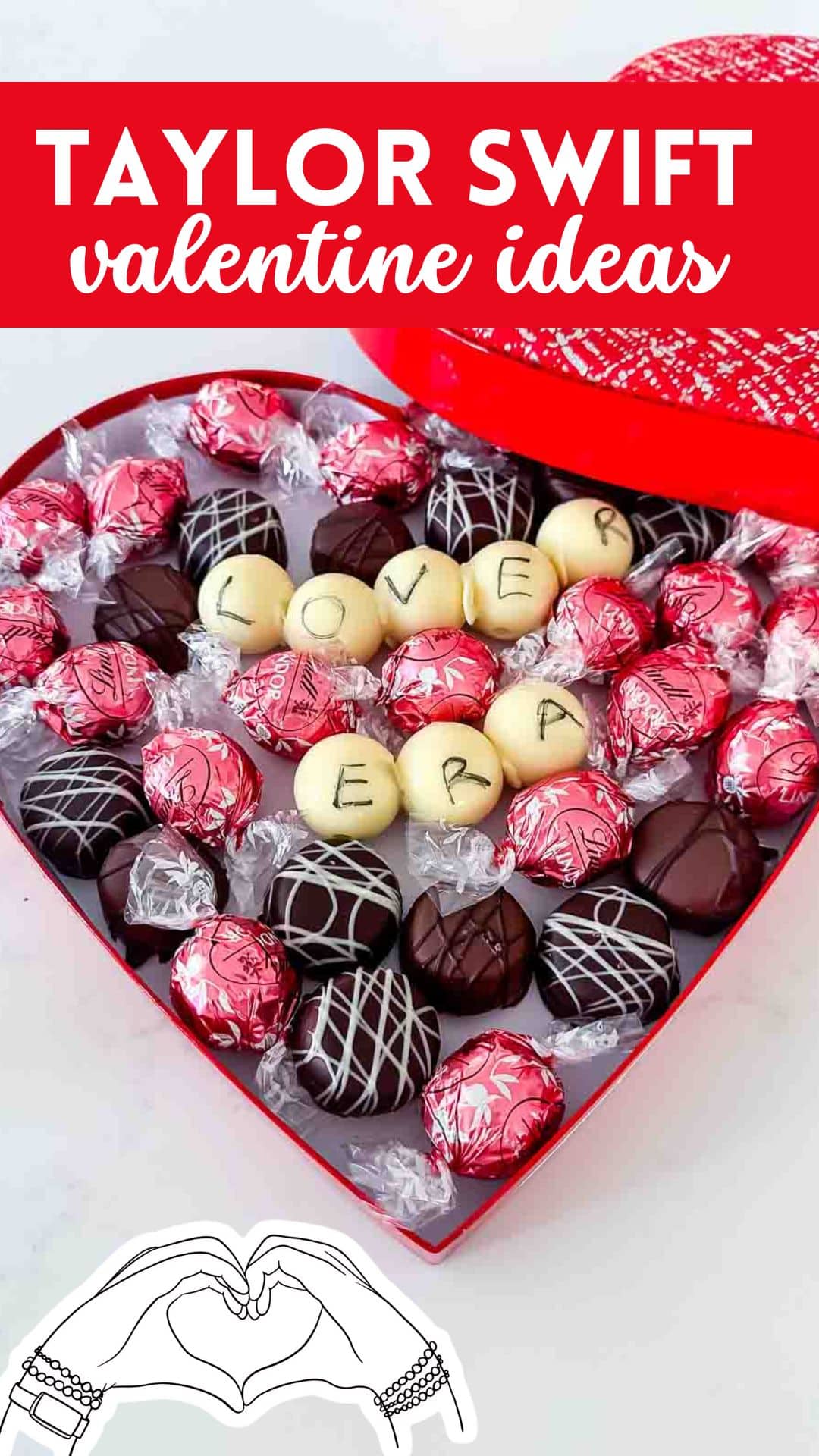 A heart-shaped box filled with assorted chocolates and candies. Some chocolates are wrapped in pink foil, and others are white with letters spelling LOVER ERA. A graphic of hands forming a heart is at the bottom. Text on top reads Taylor Swift Valentine Ideas.