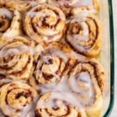 Cinnamon rolls in a glass baking dish, topped with a glossy layer of icing. The rolls are golden brown and swirled with cinnamon filling.