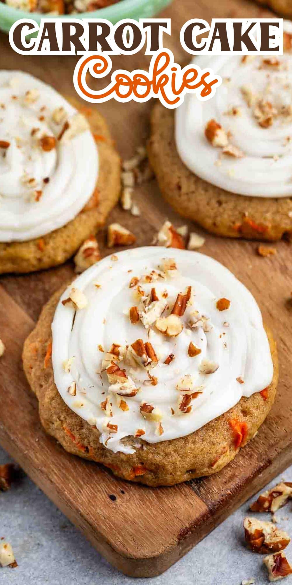 A wooden board with three carrot cake cookies topped with white frosting and chopped nuts. The text Carrot Cake Cookies is displayed at the top in a stylized font.