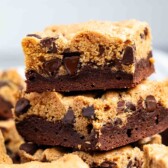 Stacked squares of brookies, a dessert combining chocolate chip cookies and brownies, are shown. The top layer is cookie dough with chocolate chips, while the bottom layer is brownie.