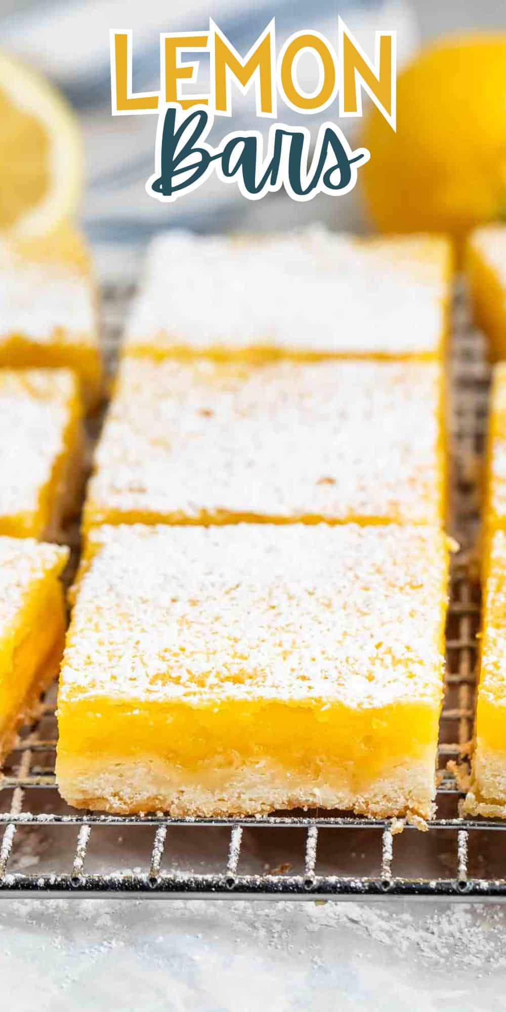 Close-up of lemon bars on a cooling rack, topped with powdered sugar. A fresh lemon is blurred in the background. The text Lemon Bars is overlaid at the top of the image.