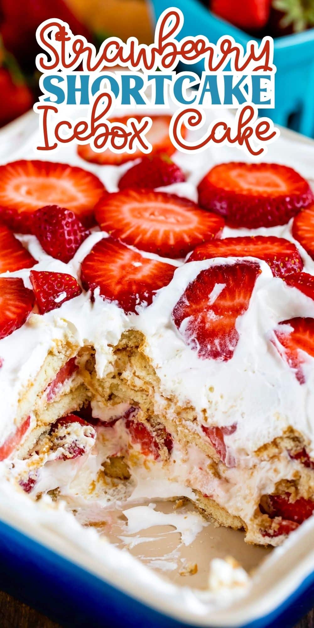 A close-up of a strawberry shortcake icebox cake with layers of whipped cream, sliced strawberries, and cake in a blue dish. The top is garnished with fresh strawberry slices. Text at the top reads Strawberry Shortcake Icebox Cake.